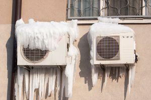 Frozen outdoor HVAC units on side of home.