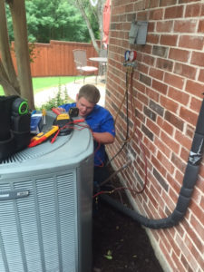 HVAC technician works on air conditioning unit outside of brick house.