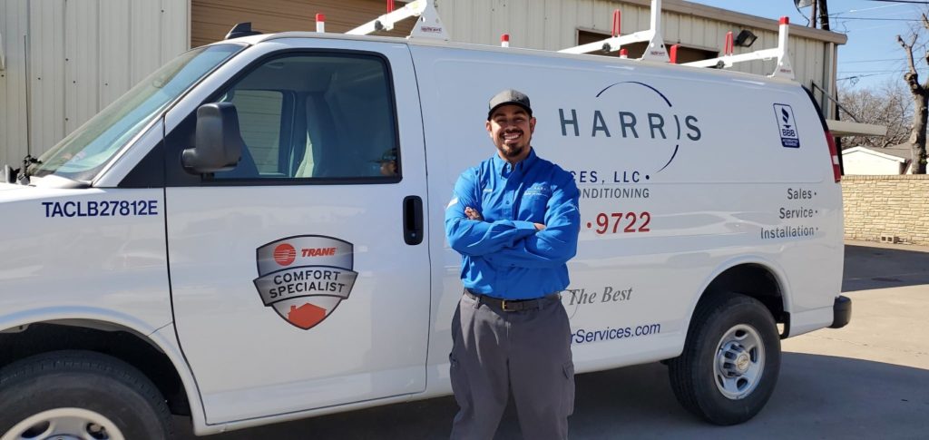 Technician with arms crossed in front of them, smiling, standing in front of Harris Air service van.