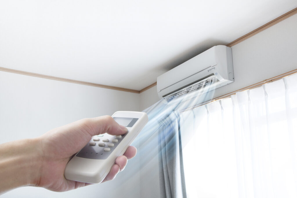 Ductless mini-split high on a wall in a home, person's hand holding remote pointed at mini-split.